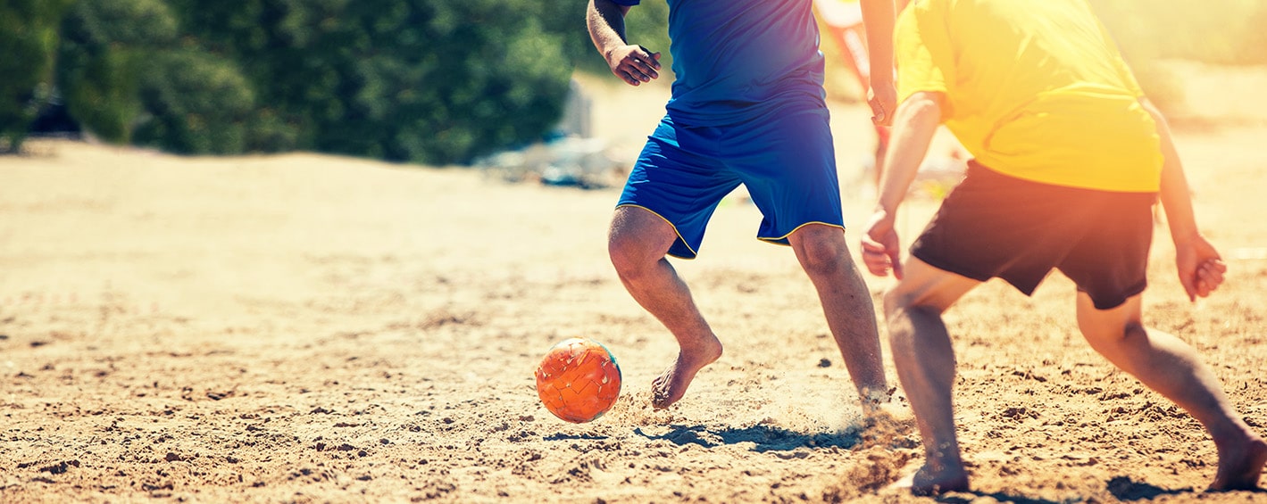 Two guys playing soccer on a beach