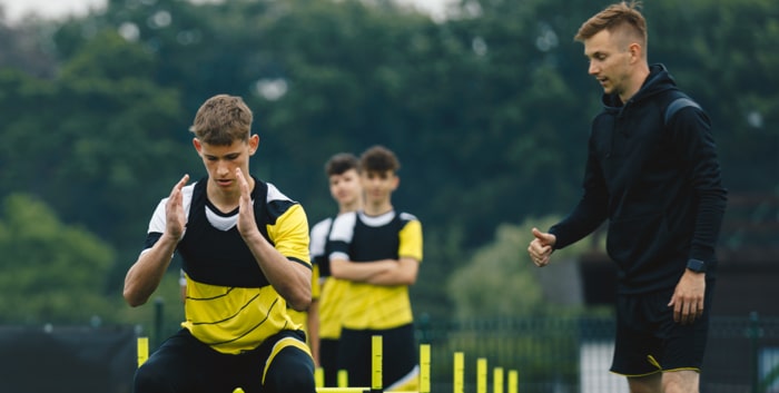 Group of Football Players on Agility Training. Young Coach Giving Advices to Player on Training.